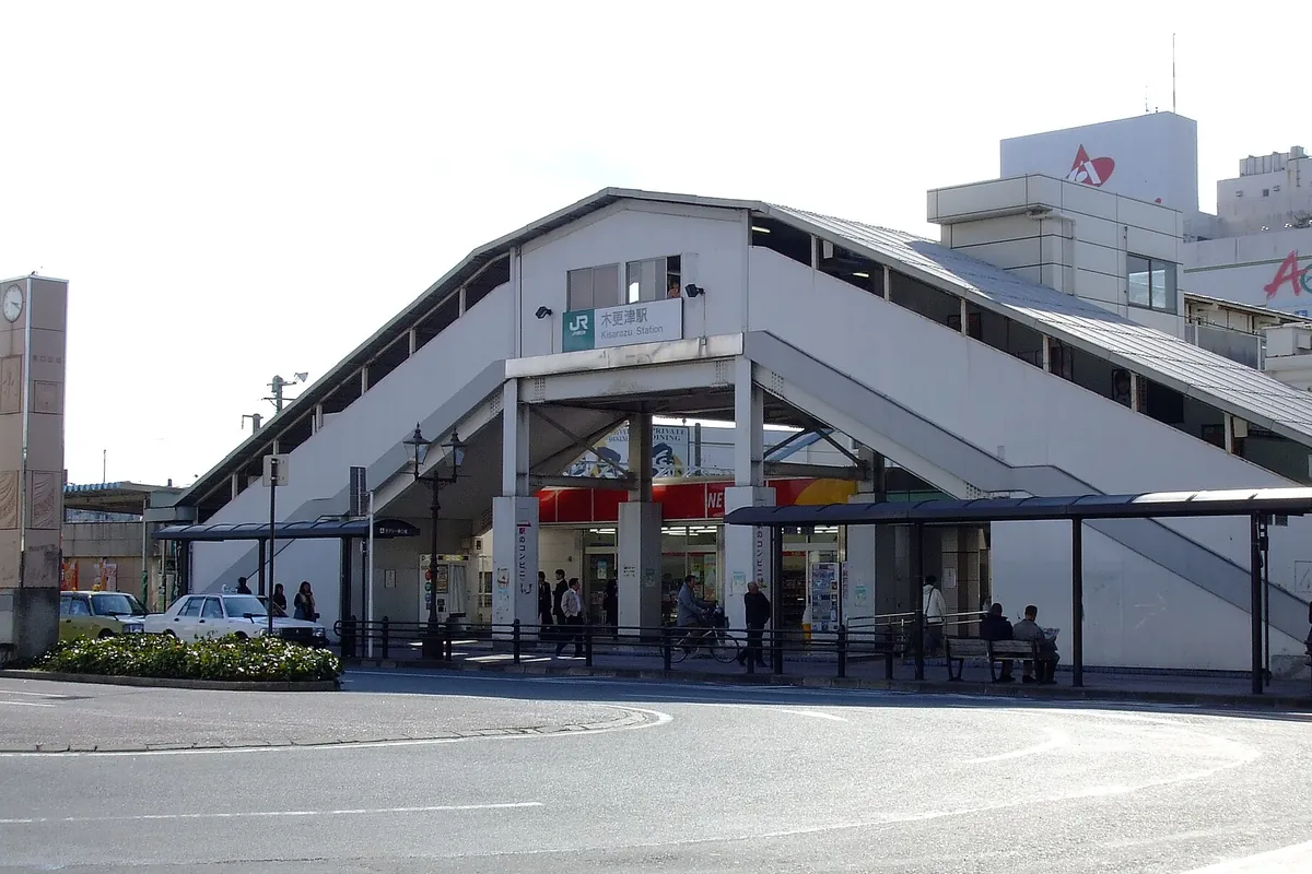 三角屋根の跨線橋とペデストリアンデッキを備えた駅舎前にタクシーやバス待合所が並ぶ木更津駅の写真