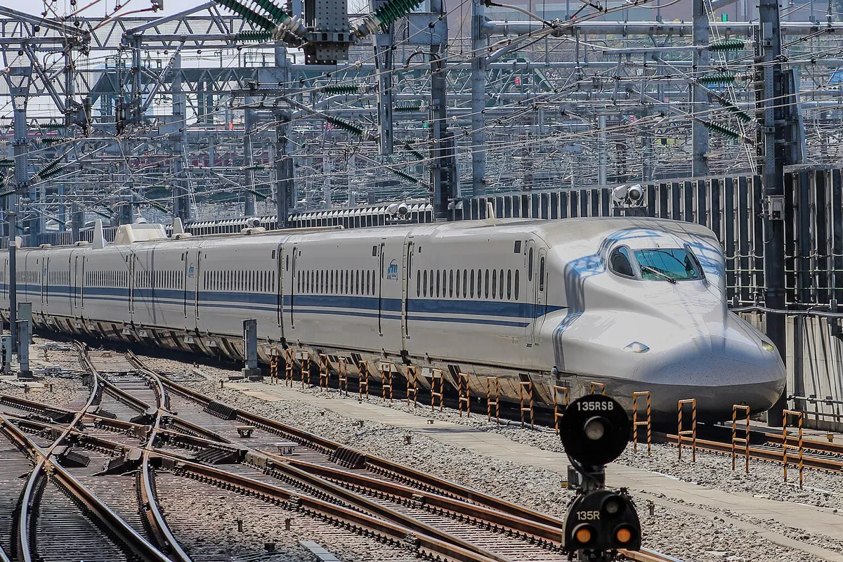 線路脇の信号機越しに走るJR東海の新幹線N700系の先頭車両を横から写した写真