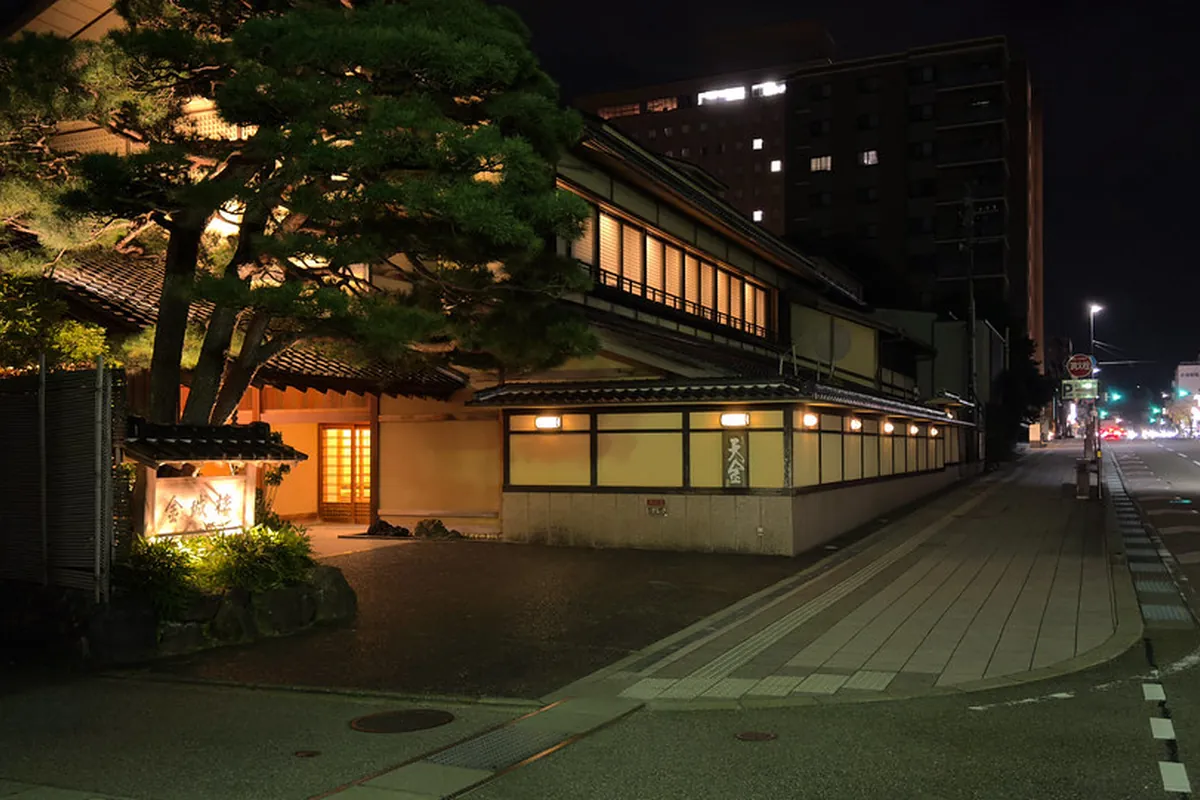 夜に明かりがともった日本旅館の玄関と看板、松の木が立つ入口の様子の写真