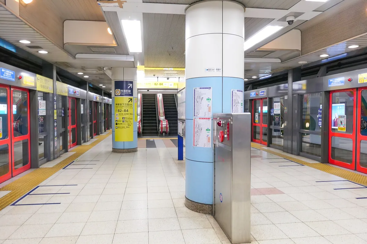 地下鉄駅のホームで、赤い扉のスクリーンドアとエスカレーター、有楽町線の案内看板が見える様子の写真