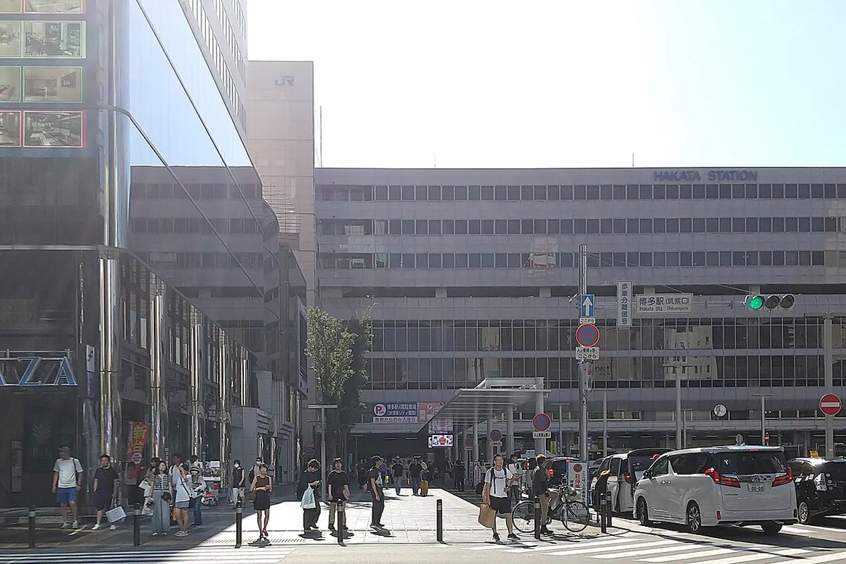 博多駅前の交差点で、信号機や案内標識の近くを歩行者や車が行き交う様子の写真