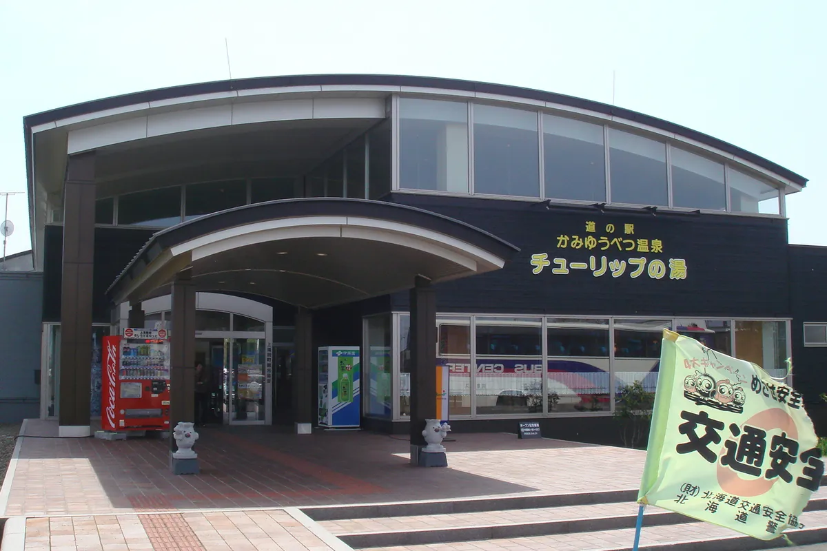 道の駅の入口に大きな庇と自動販売機があり、建物に「道の駅 かみゆうべつ温泉 チューリップの湯」と書かれた看板が掲げられている写真