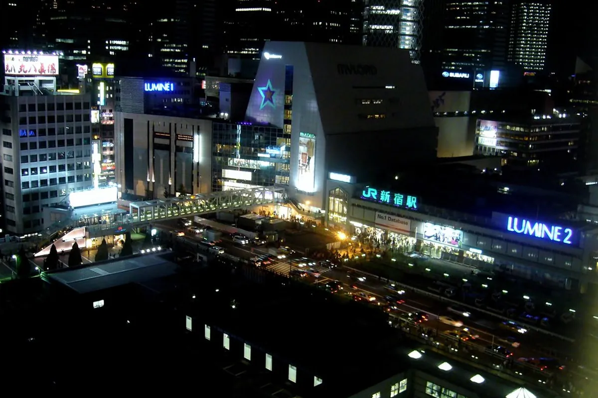 夜の新宿駅周辺で、LUMINEやビルの看板が輝く繁華街と高層ビル群を見下ろした風景の写真