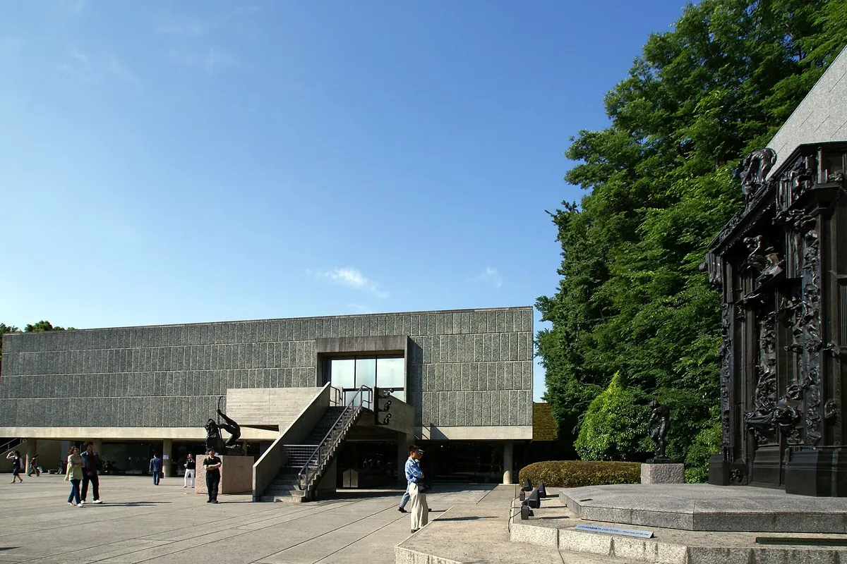 美術館の前庭に「地獄の門」の彫刻と階段のある建物が建ち、来館者が歩いている様子の写真