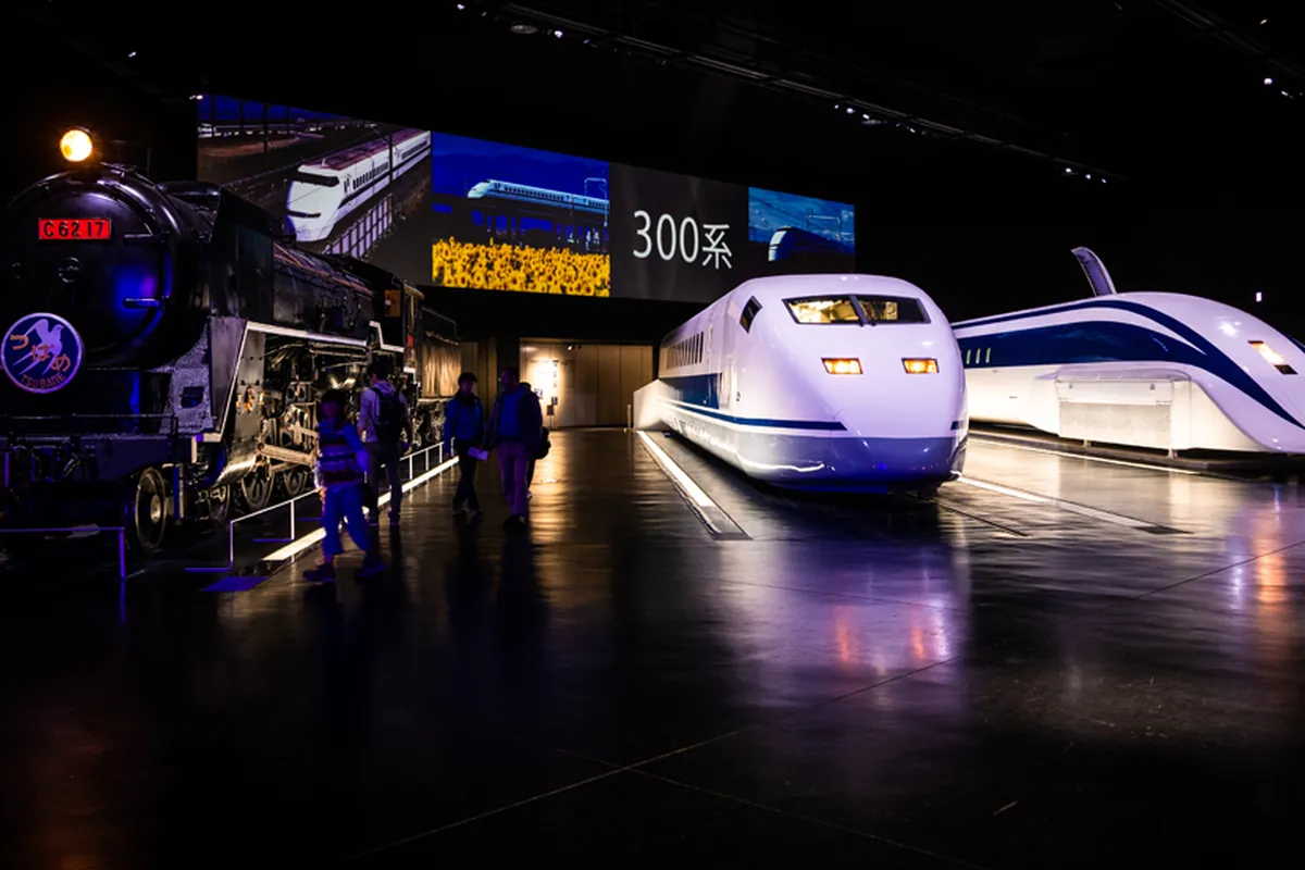 「300系」の表示の前に、黒い蒸気機関車「C62 17」と白い新幹線の車両、右奥に青い帯の鉄道車両が並ぶ展示室の写真