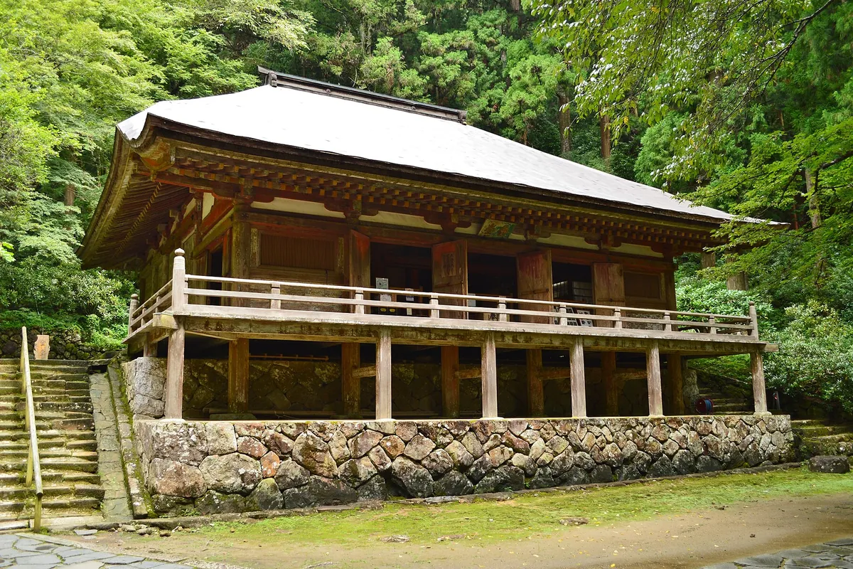 石垣の上に建つ木造の寺院建物の前に石段が続き、周囲を杉木立が囲む写真