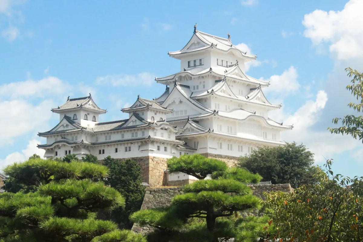 姫路城の白い天守が木々の緑と石垣の上にそびえ立つ様子の写真