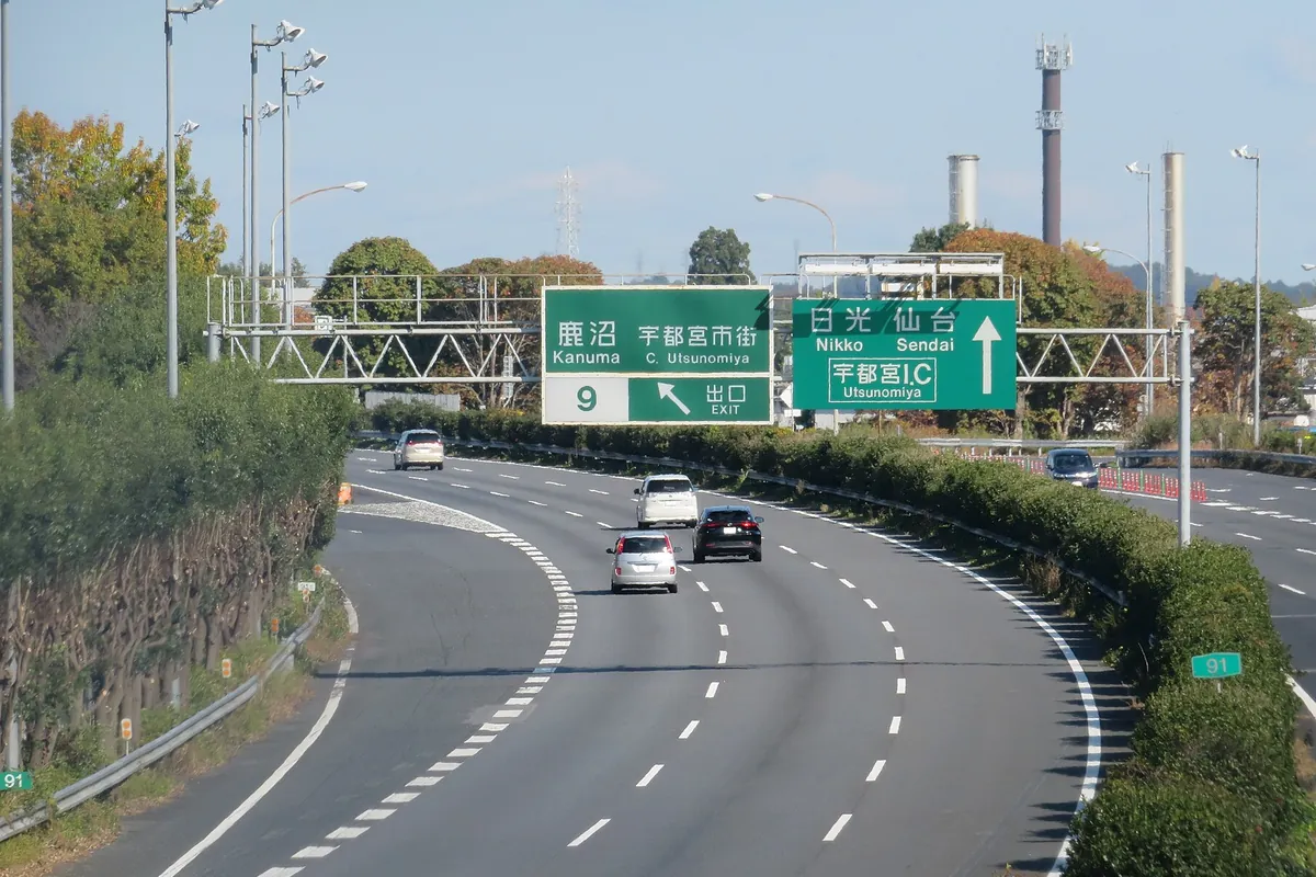 高速道路の本線上に「宇都宮I.C」「日光・仙台」などの緑色の案内標識が掲げられ、複数の乗用車が走行している様子の写真