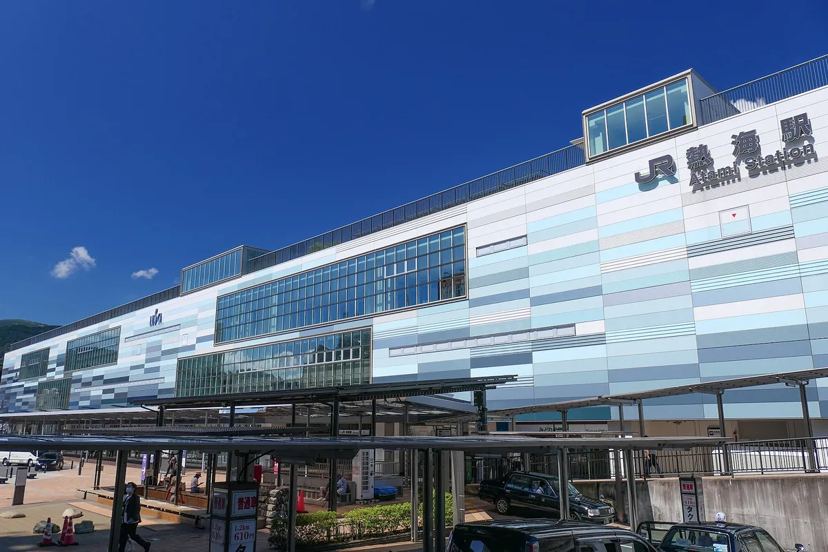 「JR熱海駅 Atami Station」の看板が掲げられた青いタイル張りの駅舎とタクシー乗り場の写真