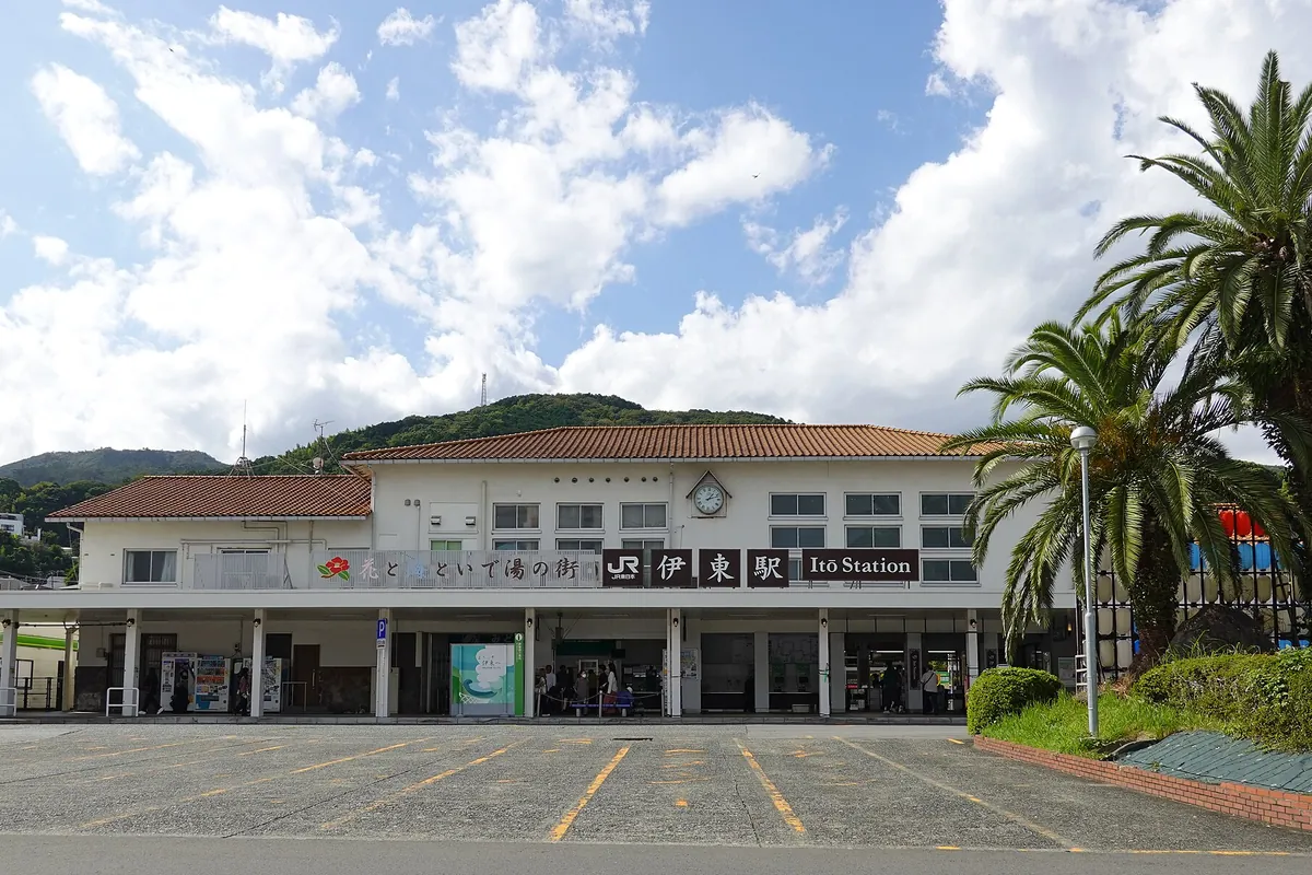 「JR東日本 伊東駅 Ito Station」の看板が掲げられた瓦屋根の駅舎とヤシの木の写真