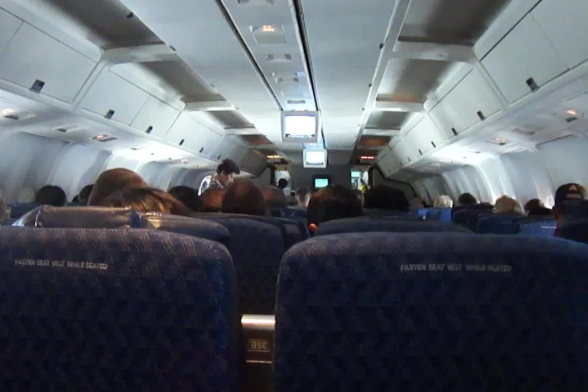 飛行機の客室内で、前方のモニターに向かって座席が並び乗客が座っている様子の写真