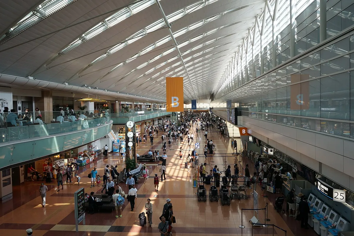 羽田空港のターミナル内で、出発ロビーに大勢の人が行き交いチェックインカウンターが並ぶ様子の写真