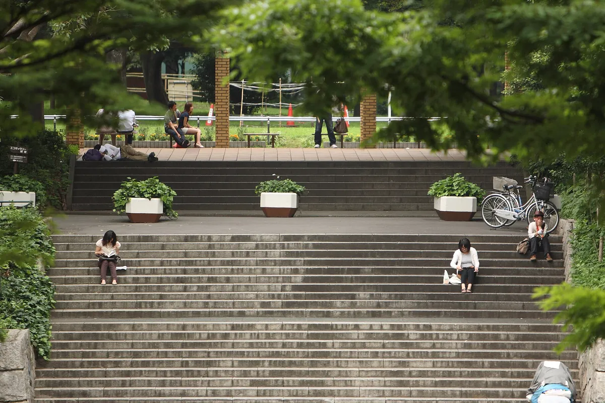 新宿区の公園で、植え込みと石段に人がまばらに座って過ごしている様子の写真