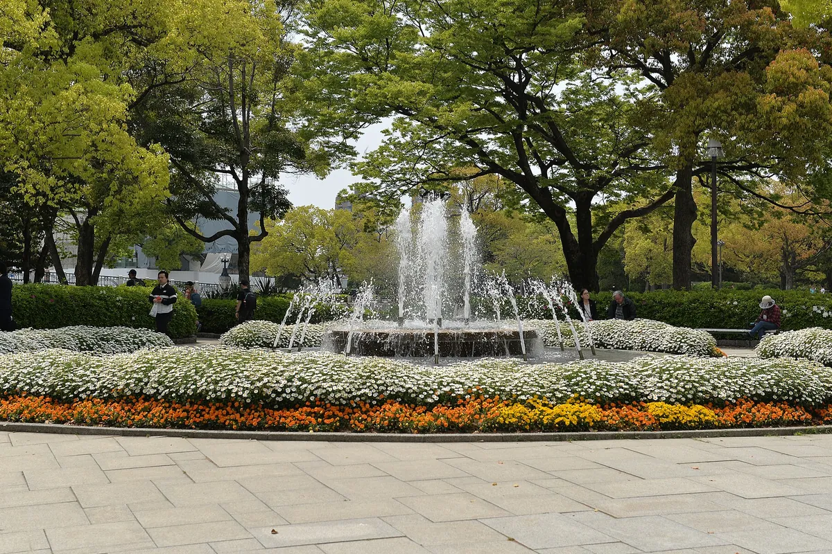 広島平和記念公園の噴水広場で、白や橙色の花壇に囲まれた噴水が水を上げている様子の写真