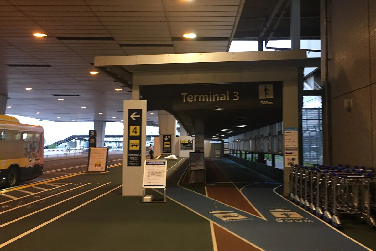 成田空港第3ターミナルへの連絡通路入口に「Terminal 3」の案内表示と案内板、カートが並ぶ様子の写真