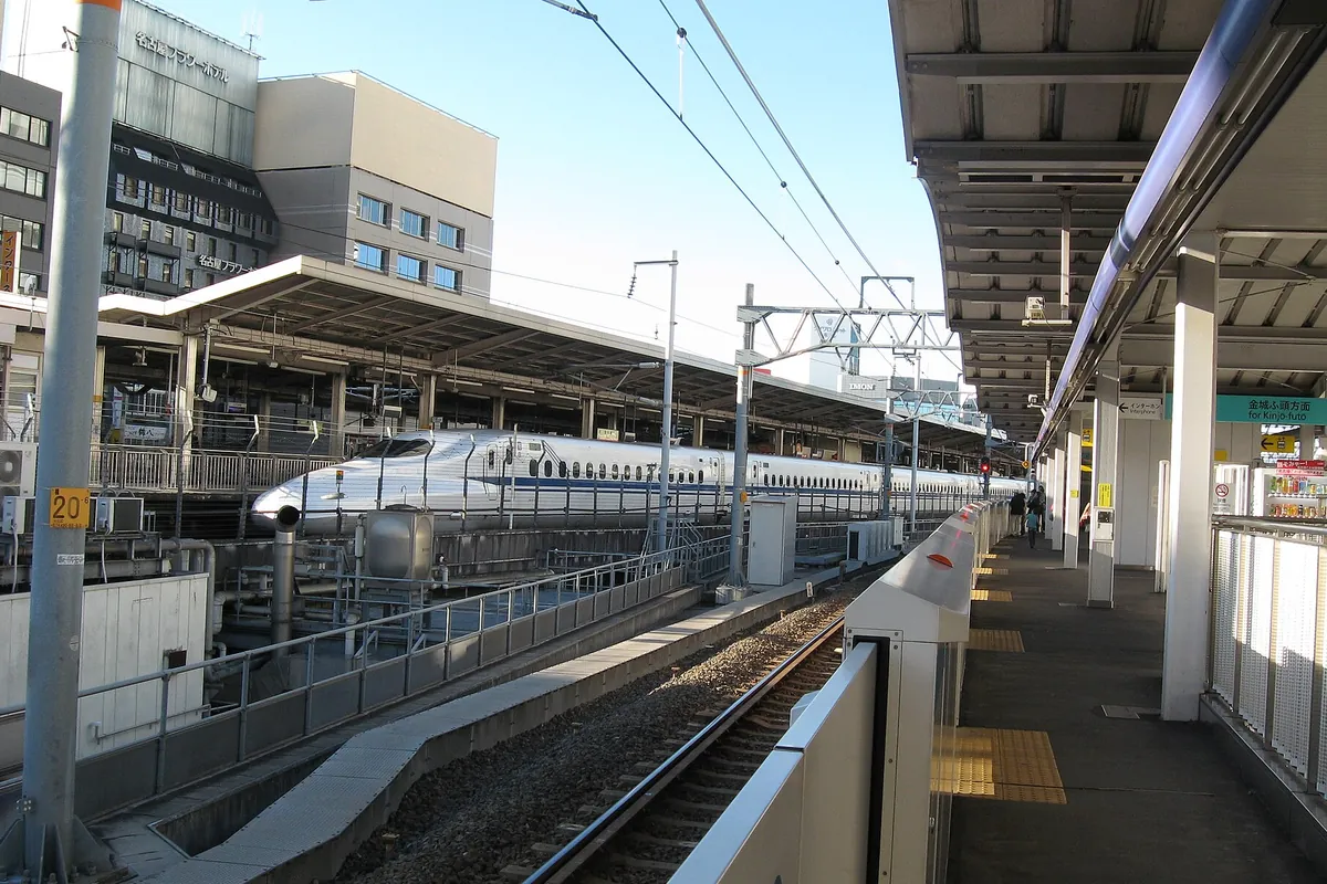 名古屋駅の新幹線ホームで、名古屋フラワーホテルなどの建物を背景に白い新幹線車両が停車している様子の写真