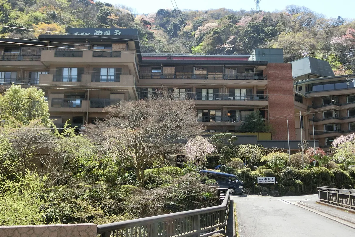 山あいに建つ温泉旅館「HOTEL NANPUSO」の建物と、周囲の木々や庭園が写る写真