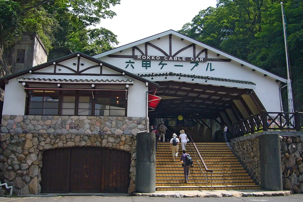 「ROKKO CABLE CAR 六甲ケーブル」の看板がある駅舎の入口で、階段を上る観光客たちが写っている写真