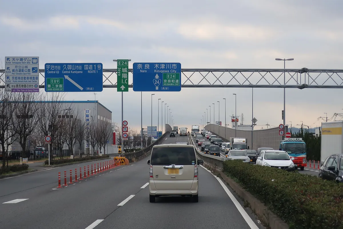 城陽インターチェンジや京奈和道方面を示す案内標識が架かる国道24号で車が連なって走る様子の写真
