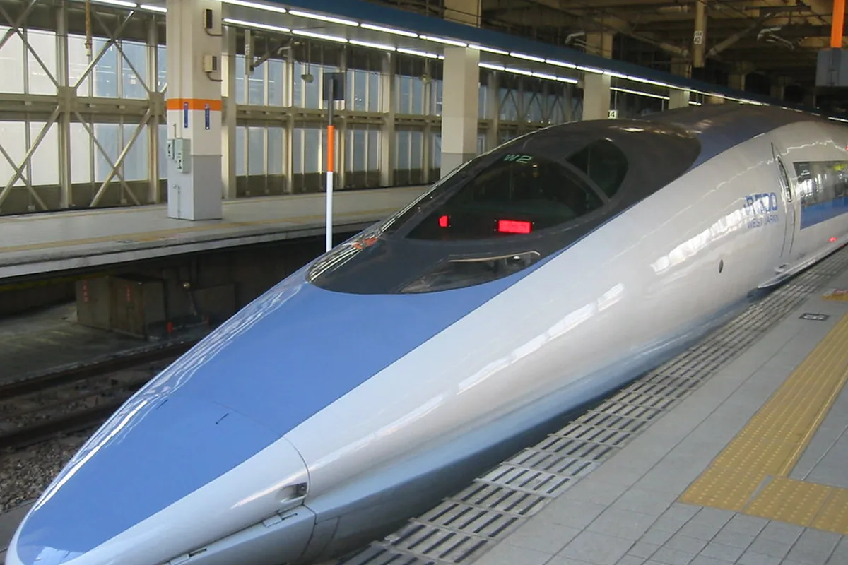 屋根のあるホームにJR西日本のロゴが入った青と白の新幹線の先頭車両が停車している写真