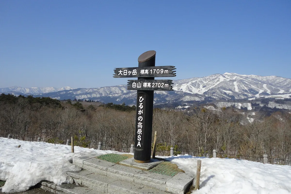 雪に覆われた展望台に「ひるがの高原SA」と書かれた標識が立ち、奥に雪山が広がる様子の写真