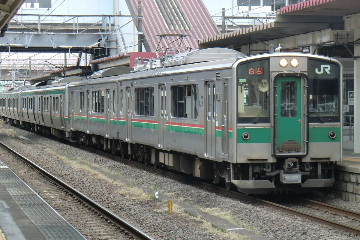緑と赤のラインが入ったJR東日本の普通列車が、屋根のあるホームに停車している様子の写真