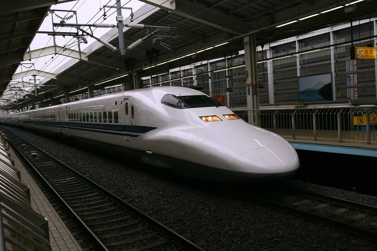 駅のホームに停車中の新幹線の先頭車両と、ホーム屋根や「出口」の案内表示が見える構内の写真。