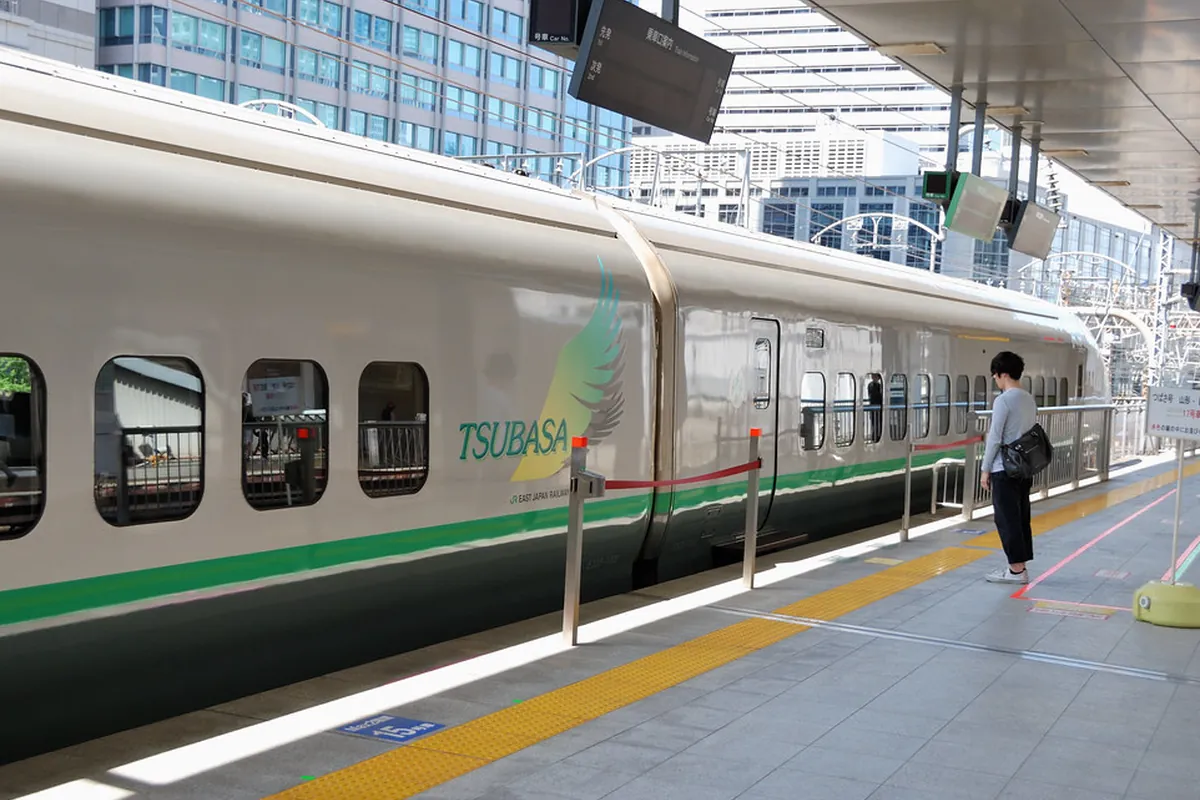 新幹線のホームに停車する緑色のラインが入った山形新幹線「つばさ」の車両と、乗車を待つ利用客の写真
