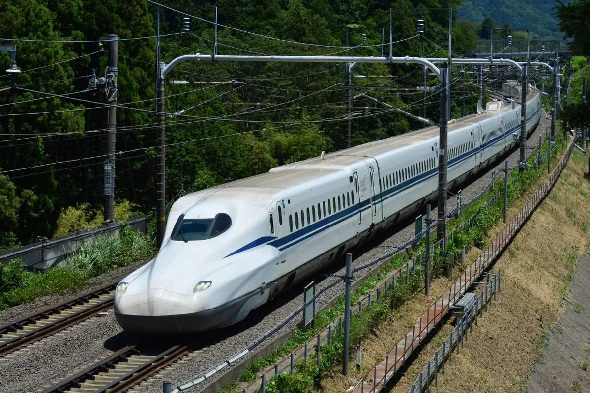 緑に囲まれた線路を走る青いラインの入った白色の東海道新幹線の車両の写真