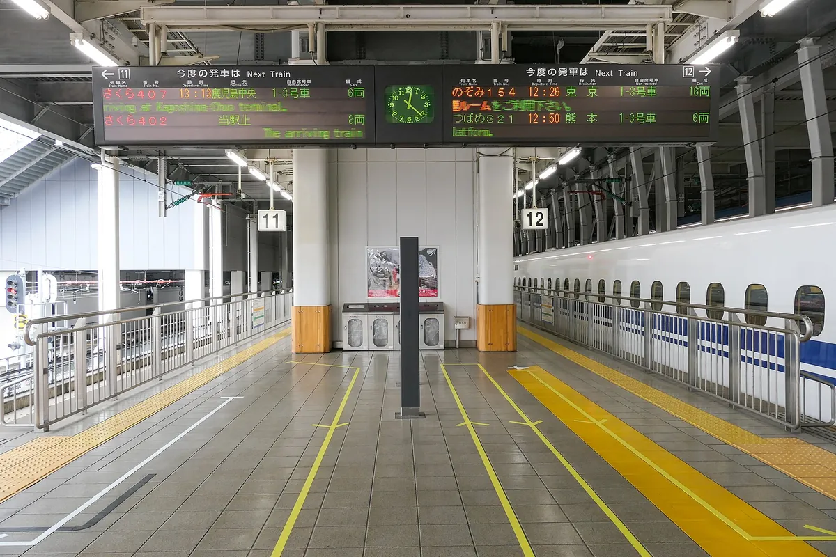 新幹線ホームで発車案内板に「さくら」「のぞみ」「つばめ」の列車名が表示され、白い新幹線車両が停車している様子の写真