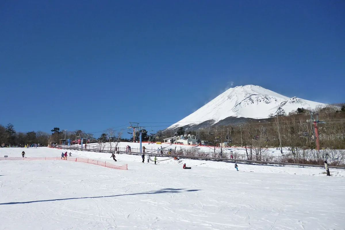 雪原の先に雪をかぶった富士山がそびえ、リフトやゲレンデで多くの人がスキーやスノーボードを楽しむ様子の写真