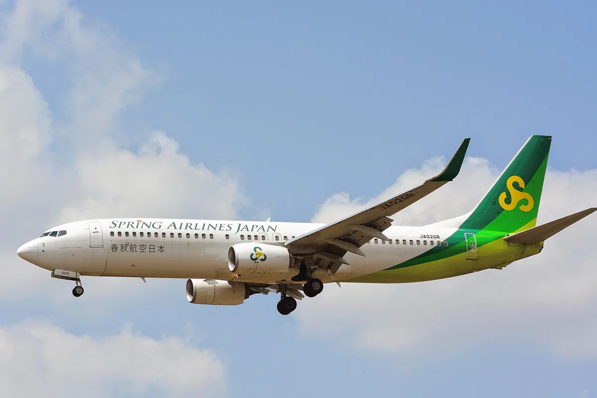 スプリング・ジャパンの緑と黄色の尾翼が入ったボーイング737-800が、青空を背景に飛行する様子の写真