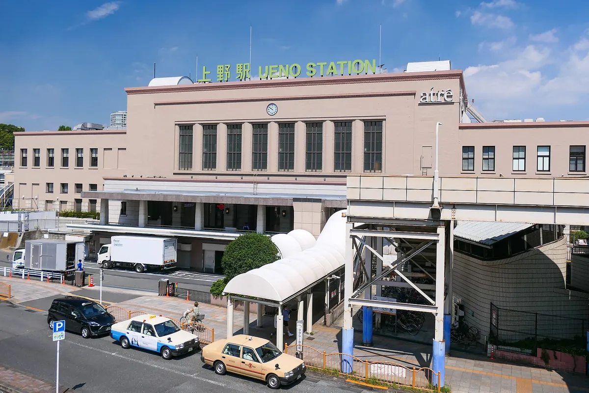 「上野駅 UENO STATION」の看板が掲げられたJR上野駅の駅舎外観と、前の道路にタクシーが停まる様子の写真