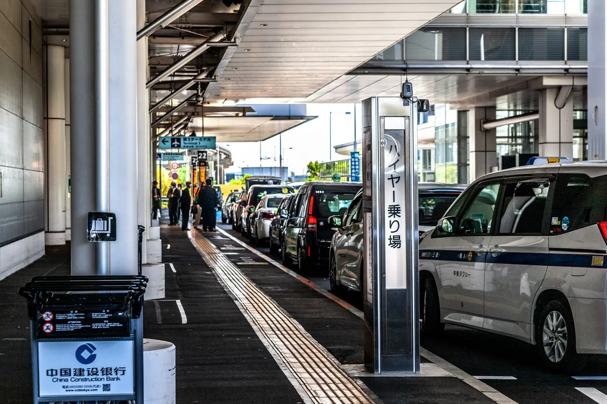羽田空港のターミナルで「ハイヤー乗り場」の案内柱の横にタクシー車両が並ぶ様子の写真