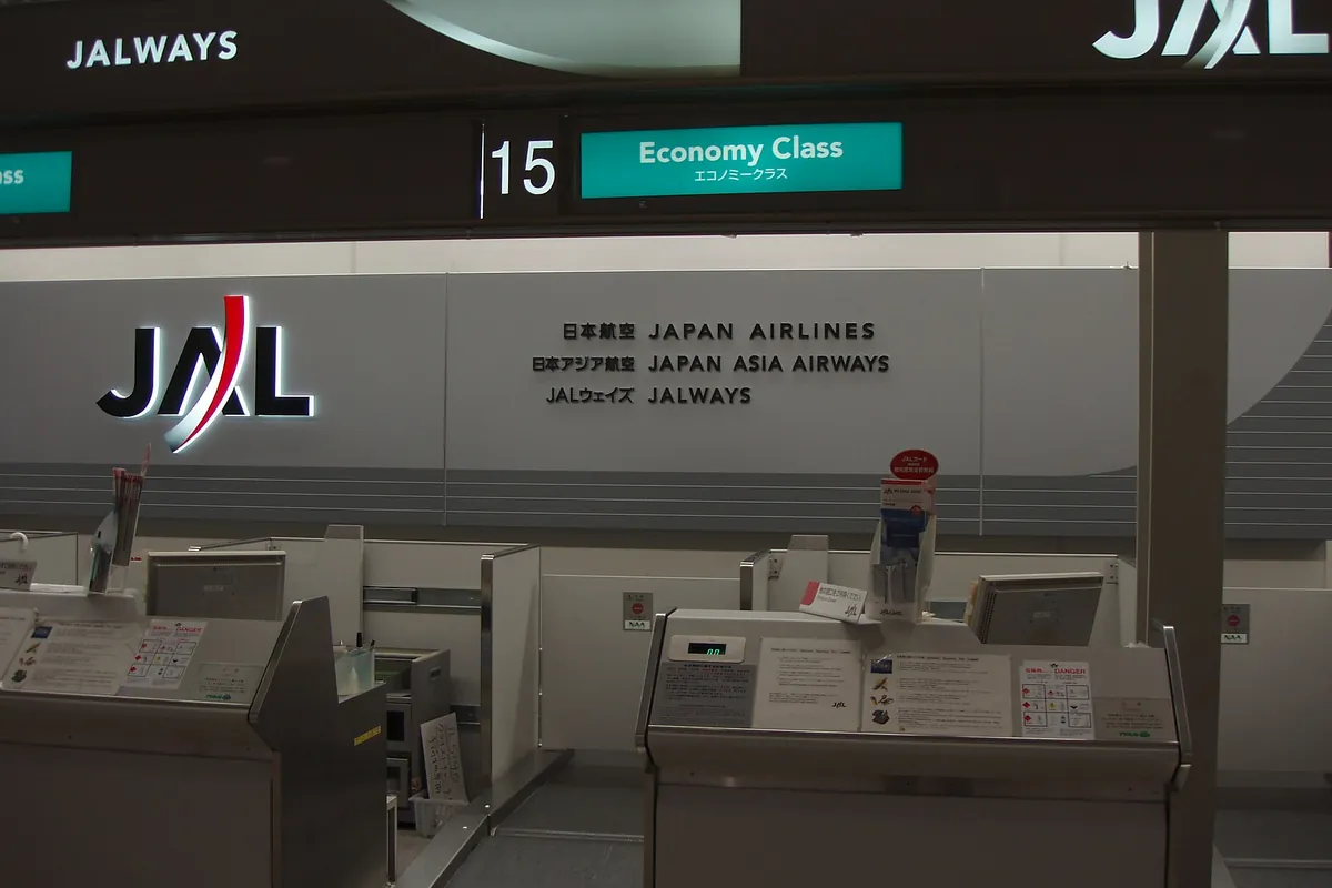 空港の国内線出発カウンターで、「JAPAN AIRLINES」の表示とJALのロゴが掲げられた様子の写真