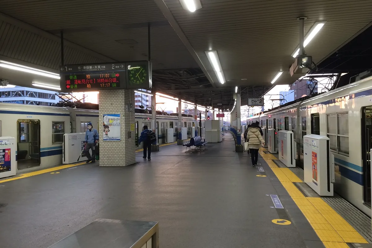 駅のホームで「柏」行きの発車案内が表示され、電車と乗客が写る様子の写真