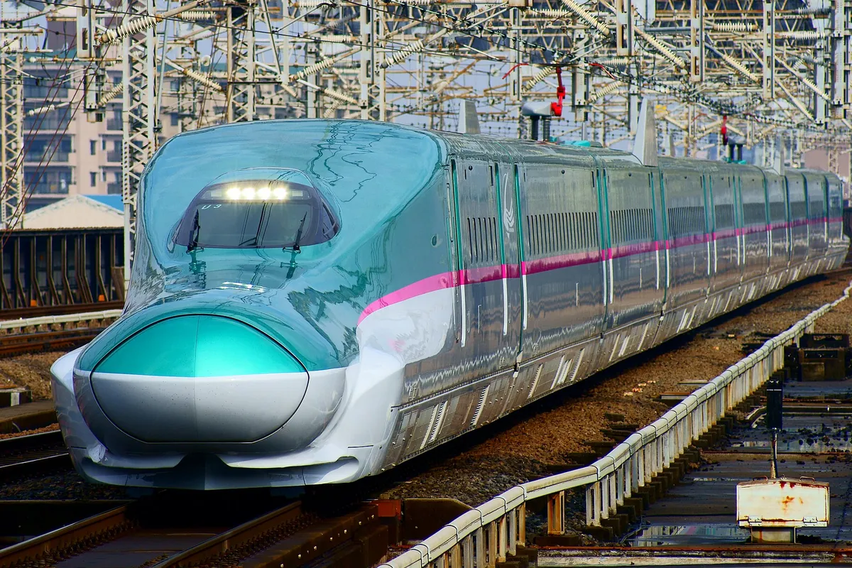 東京駅のホームに停車する緑とピンクの帯の東北新幹線はやぶさ号の先頭車両の写真
