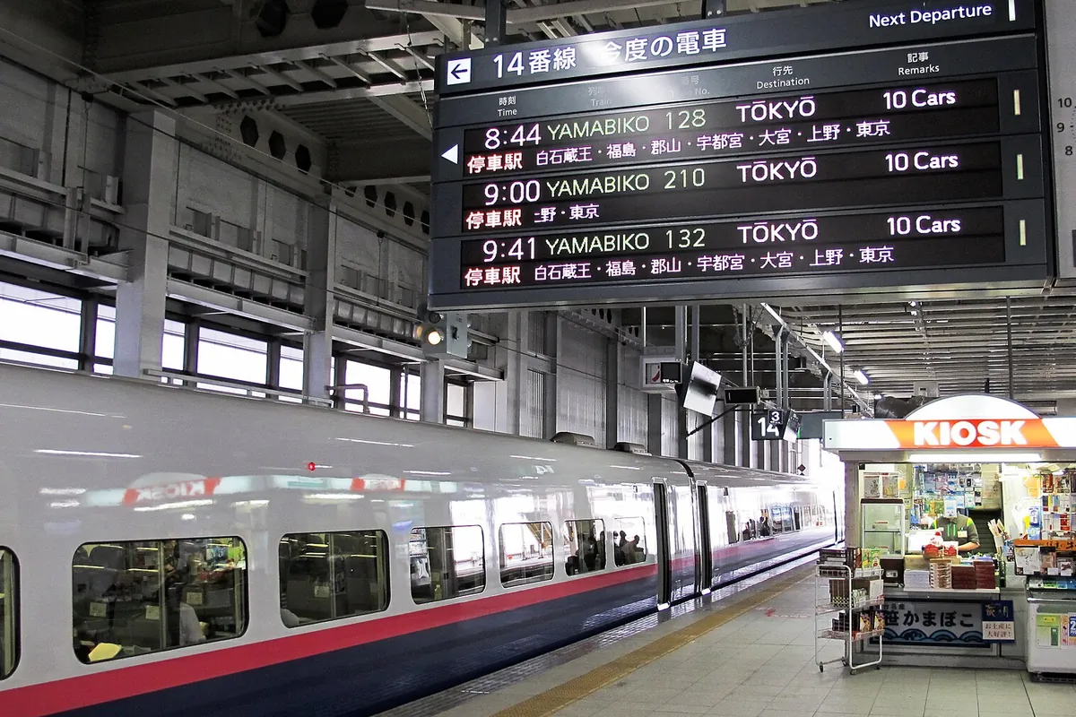 新幹線ホームで「やまびこ」東京行きの発車案内表示板とキオスク、白い新幹線車両が写る写真