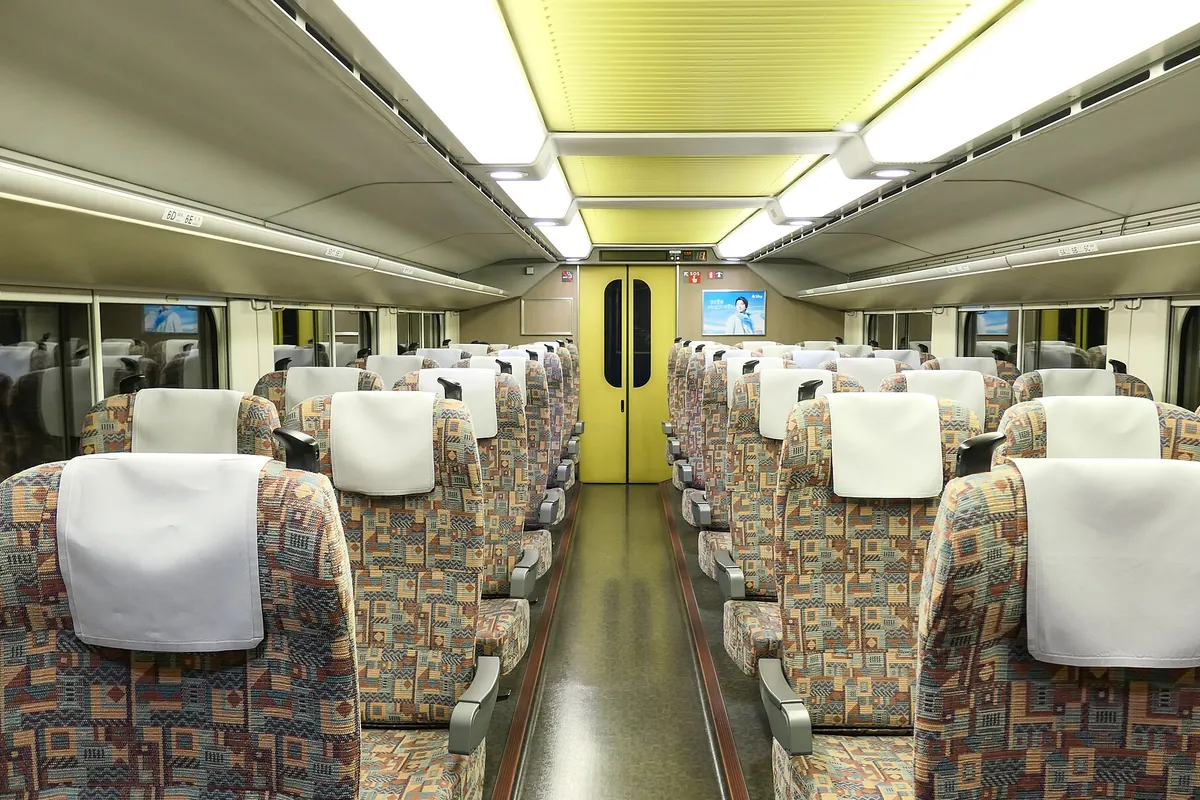 東北新幹線の自由席車内で、模様入りの座席と黄色いドアが並ぶ通路の写真