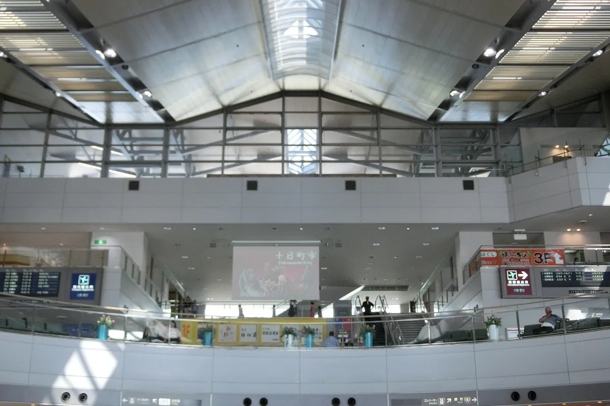 空港ターミナル内の吹き抜けで、上階から案内表示板やエスカレーターを見下ろした様子の写真