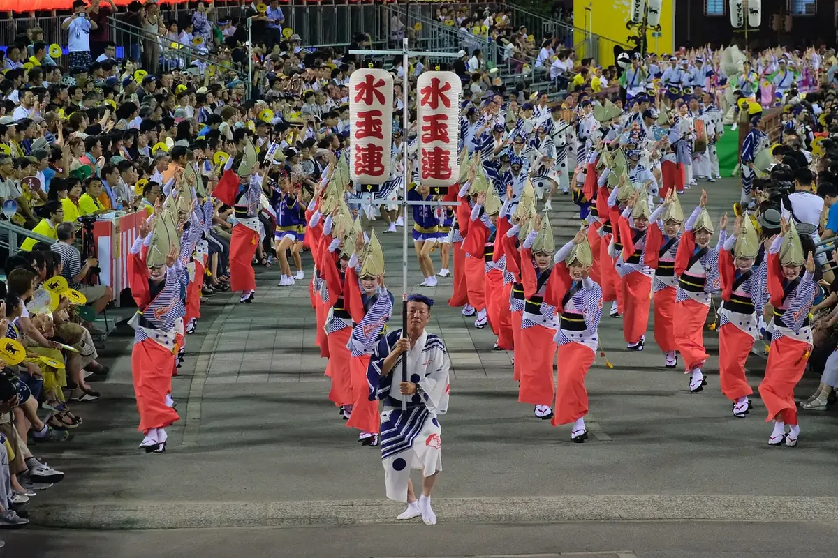 阿波おどりの演舞場で、編み笠をかぶった着物の踊り手たちが提灯を先頭に列になって踊り進む様子の写真