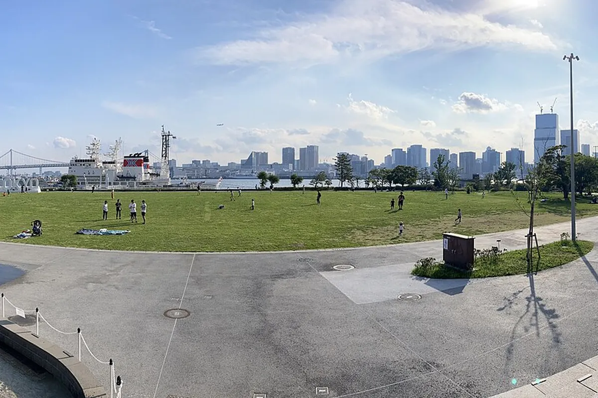 晴海ふ頭公園の芝生広場で人々が過ごし、背景にレインボーブリッジとビル群が広がる景色の写真