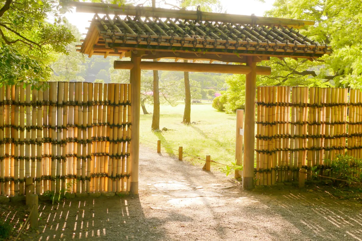 竹垣に囲まれた木造の門をくぐると芝生の庭園が広がる様子の写真