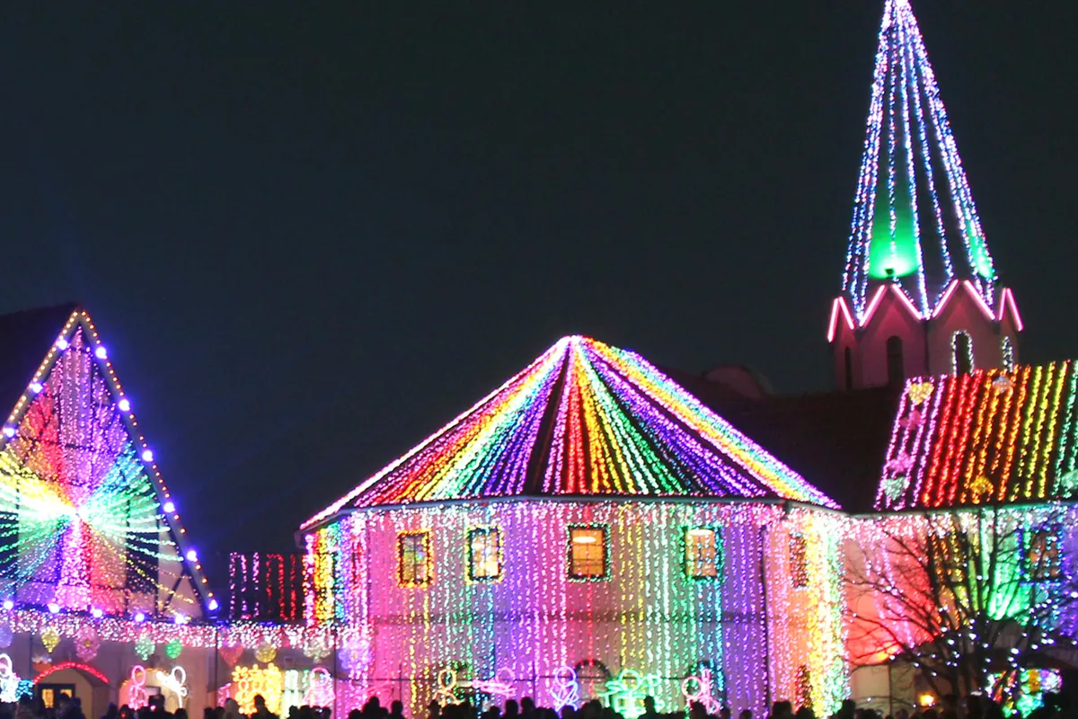 夜にライトアップされた東京ドイツ村のイルミネーションで、三角屋根の建物と尖塔がカラフルな光に包まれている写真