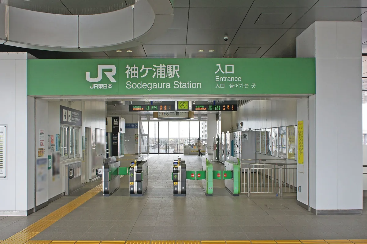 JR袖ケ浦駅の入口に緑色の駅名看板が掲げられ、自動改札機が並ぶ様子の写真