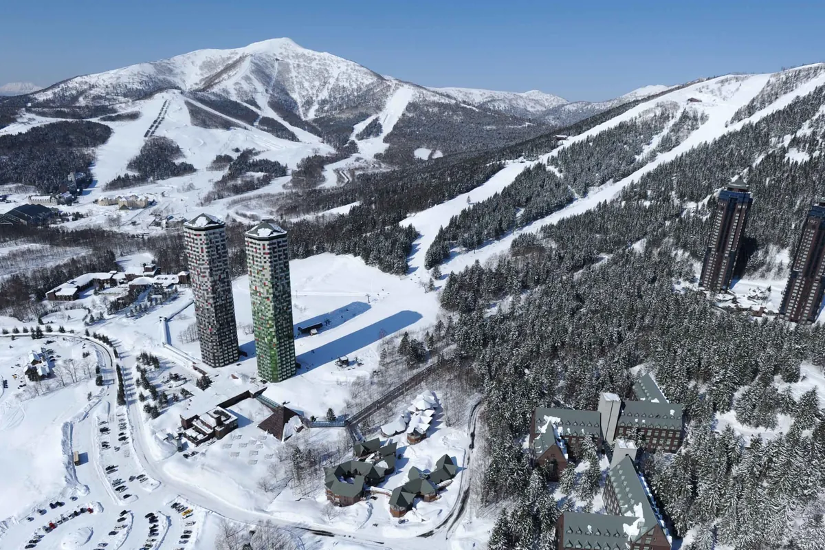 雪に覆われた山を背景に、高層タワー2棟と周辺の宿泊施設が並ぶトマムリゾートを上空から見た写真