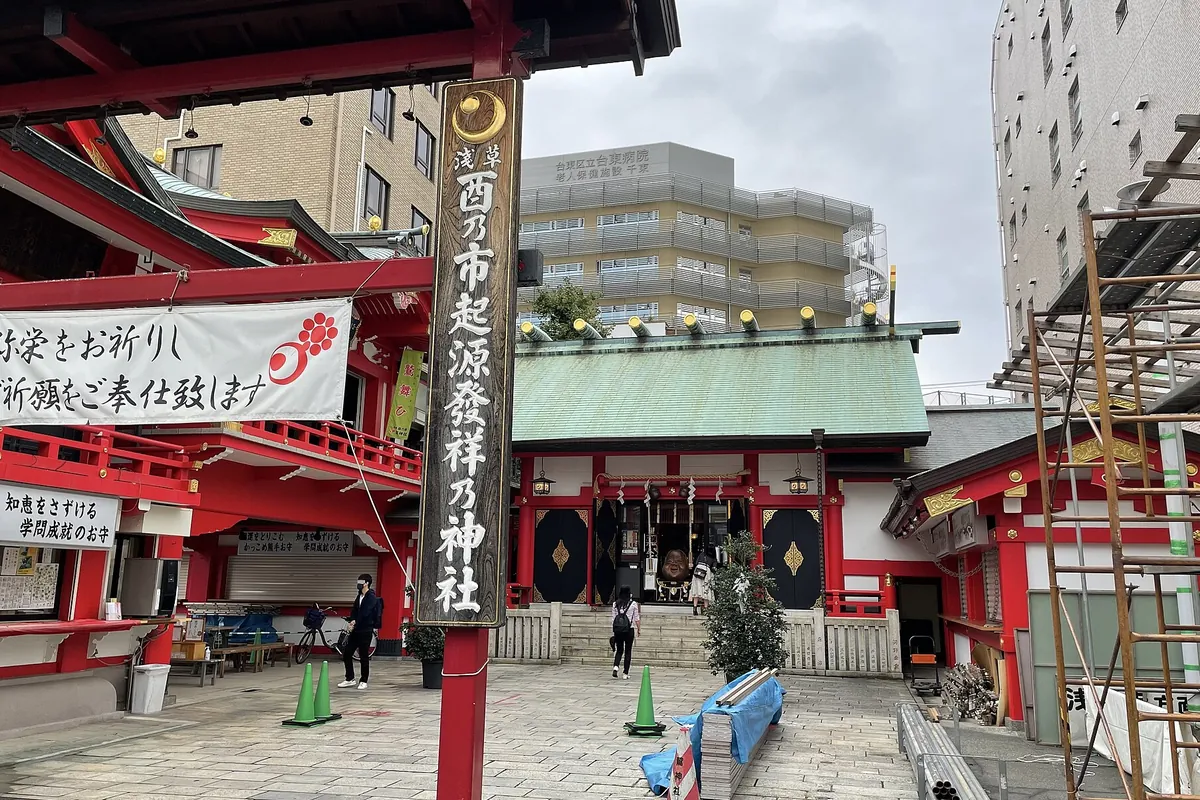 浅草の鷲神社で「酉乃市起源發祥乃神社」と書かれた木柱の奥に、朱塗りと緑屋根の社殿が建つ様子の写真