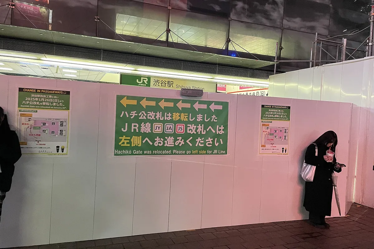 JR渋谷駅前の仮囲いに「JR渋谷駅」の看板と改札の移転を知らせる案内板が貼られ、通行人が一人立っている写真