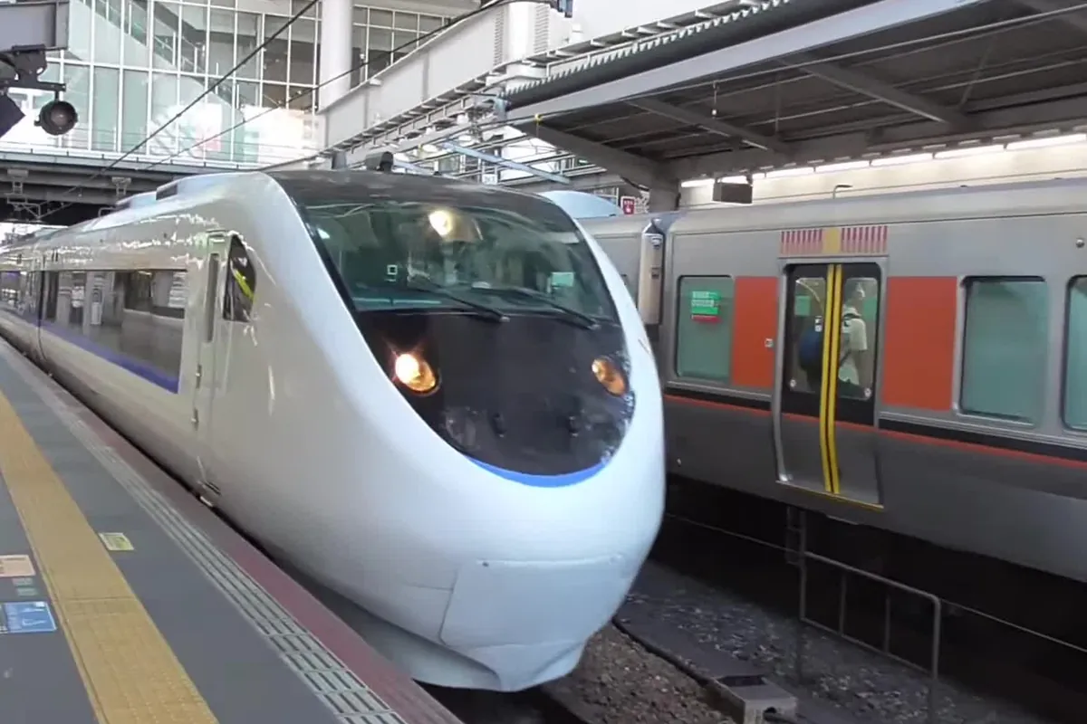 駅のホームに停車する、白い車体に青い帯が入った特急サンダーバードの先頭車両と隣の在来線車両の写真