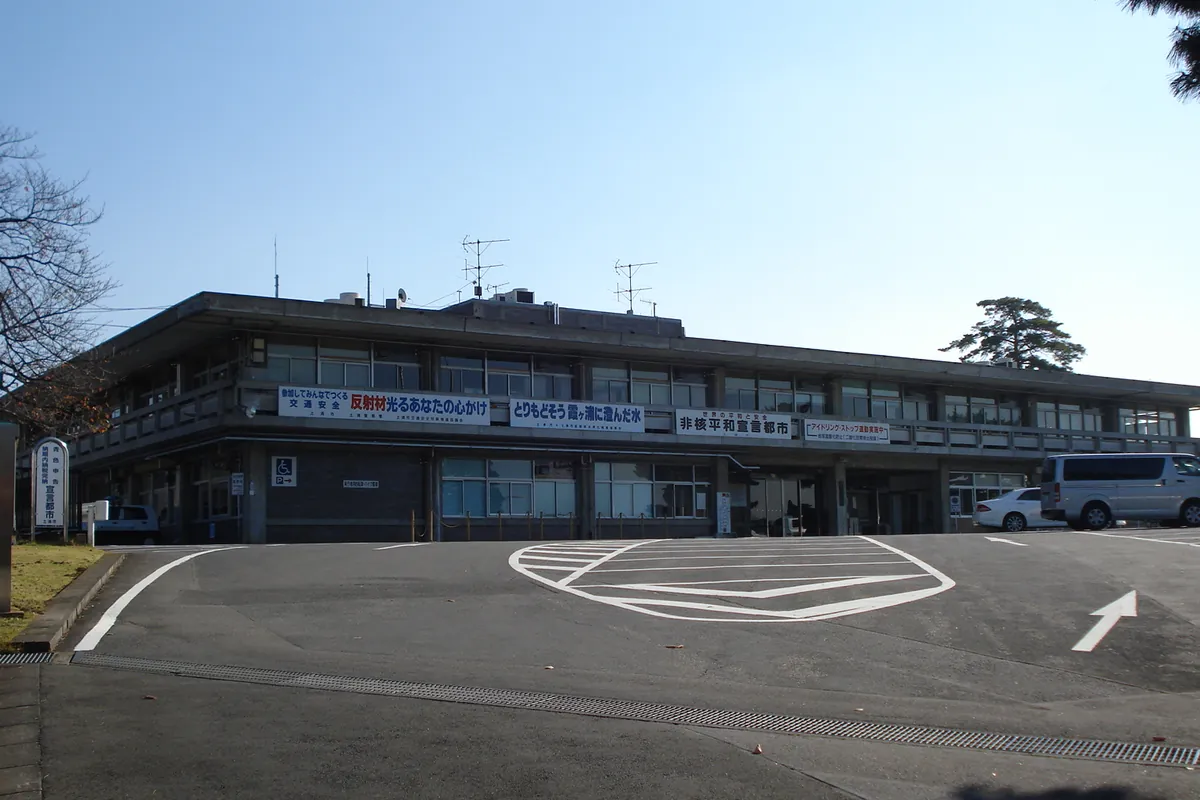 「非核平和宣言都市」などの横断幕が掲げられた2階建ての土浦市役所庁舎と駐車場の様子を写した写真